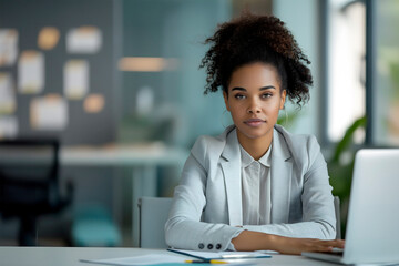 Portrait of black confident young woman, businesswoman,executive director,boss,sitting at office desk with laptop in business suit,looking at camera with her hands folded,concept of business materials