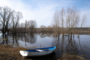 An empty boat on the shore of the overflowing floodplain of the river in spring.