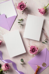 Flat lay composition with blank wedding invitation cards, purple envelopes, roses on marble desk table. Top view.