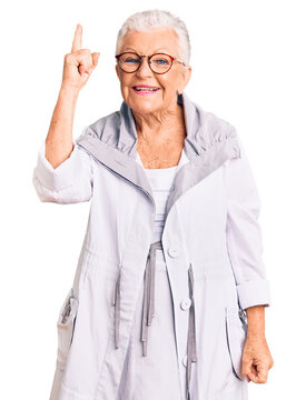 Senior beautiful woman with blue eyes and grey hair wearing casual clothes and glasses pointing finger up with successful idea. exited and happy. number one.