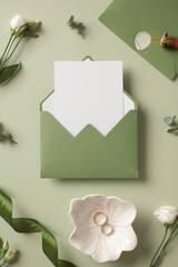 Craft paper envelope with blank paper card on green background. Wedding invitation mockup. Top view.