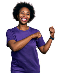 African american woman with afro hair wearing casual purple t shirt pointing to the back behind...