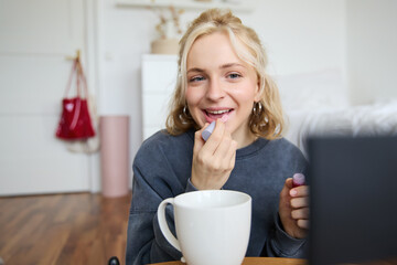 Lifestyle, beauty blogger, woman recording video of her putting on makeup, talking to camera,...