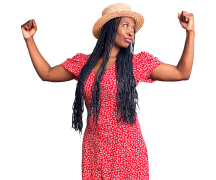 Young african american woman wearing summer hat showing arms muscles smiling proud. fitness concept.