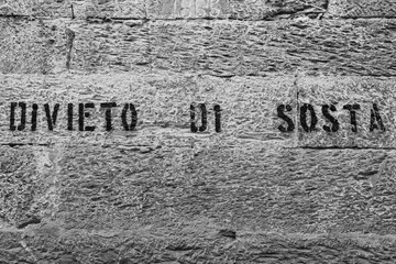 Black and white photo of a concrete wall with the inscription "no parking" in Italian