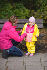 A mother is putting a yellow rainjacket on her little girl and a girl is holding rowanberries in her hand. Pink and yellow kids outfit. Vertical image.