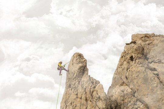 A person is standing on a rock with a yellow and green rope. The person is smiling and he is enjoying the experience. Concept of adventure and excitement. On fluffy clouds.