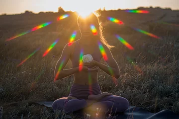 Wandcirkels aluminium Beautiful girl - yoga in the lotus position with a white rose against the background of dawn with rainbow highlights © Vladimir Bartel
