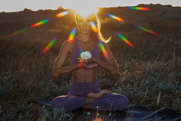 Beautiful girl - yoga sits on the grass in the lotus position with a white rose against the...