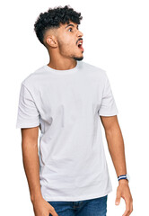 Young arab man wearing casual white t shirt angry and mad screaming frustrated and furious, shouting with anger. rage and aggressive concept.