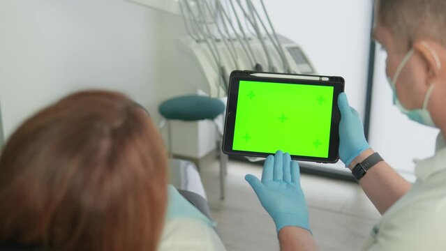 The dentist shows the patient a green screen tablet, dismantles the information. Template layout to insert an image or video. Dental clinic at the doctor's office