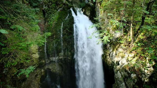 A powerful narrow waterfall, coming out of a natural high gorge, that surrounded by lush greenery and rocks. a 4K video clip.