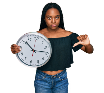 Young african american woman holding big clock with angry face, negative sign showing dislike with thumbs down, rejection concept