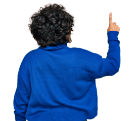 Young hispanic woman with curly hair wearing turtleneck sweater posing backwards pointing ahead with finger hand