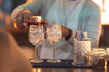 A man is pouring a drink into two glasses on a bar