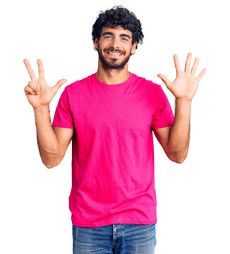 Handsome young man with curly hair and bear wearing casual pink tshirt showing and pointing up with fingers number eight while smiling confident and happy.