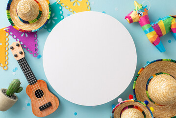 Top angle view of Cinco de Mayo-inspired items: sombreros, a vihuela, cactus in a pot, flag streamers, pinata, and confetti, all set against a pastel blue backdrop with empty circle
