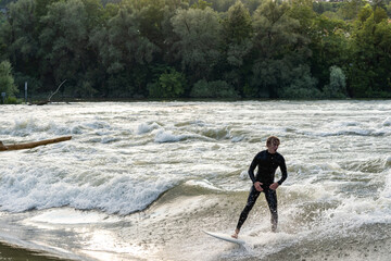 A young surfer wearing a wetsuit surfs in the Aare river during high tide.