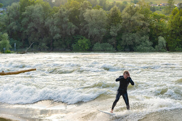 A young surfer wearing a wetsuit surfs in the Aare river during high tide.