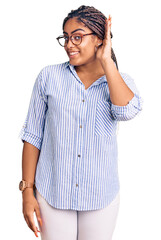 Young african american woman with braids wearing casual clothes and glasses smiling with hand over ear listening an hearing to rumor or gossip. deafness concept.