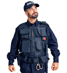 Young hispanic man wearing police uniform smiling looking to the side and staring away thinking.