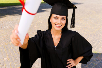 Hermosa jóven se acaba de graduar, vestida con su traje de graduación y su sombrero exhibe su diploma. Su carrera universitaria fue exitosa y su esfuerzo fue muy grande pero aquí está la recompensa.