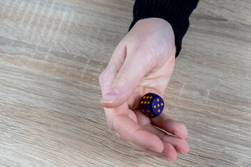 Hand of a young Caucasian woman throwing a purple dice