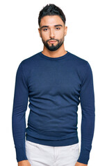 Young man with beard wearing casual blue winter sweater with serious expression on face. simple and...