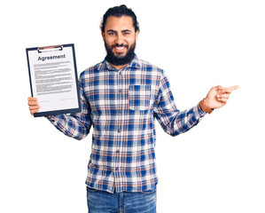 Young arab man holding clipboard with agreement document smiling happy pointing with hand and...