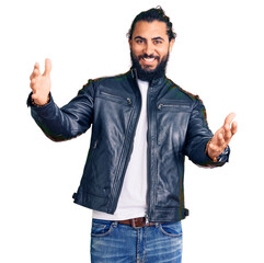 Young arab man wearing casual leather jacket looking at the camera smiling with open arms for hug. cheerful expression embracing happiness.