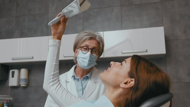 Dental Consultation: Woman Admiring Teeth in Mirror as Dentist Explains Procedure