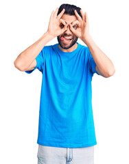 Young handsome man with beard wearing casual t-shirt doing ok gesture like binoculars sticking tongue out, eyes looking through fingers. crazy expression.