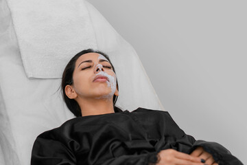 Latina woman lying down with white mask residue on her face. Facial treatment.