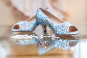 Bridal diamond engagement ring on reflective surface with soft focus of jewelry shoes and gown in the background