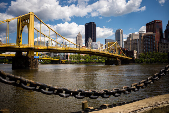 Yellow Andy Warhol Bridge spans the Allegheny River with downtown Pittsburgh behind on a sunny day.