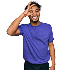 Young african american man with beard wearing casual purple t shirt doing ok gesture with hand smiling, eye looking through fingers with happy face.