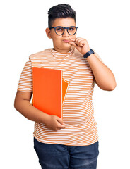 Little boy kid holding book wearing glasses mouth and lips shut as zip with fingers. secret and...