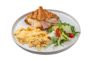 breakfast with croissant, ham, scrambled eggs and greens on an isolated white background in a plate