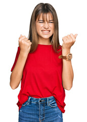 Teenager caucasian girl wearing casual red t shirt angry and mad raising fists frustrated and furious while shouting with anger. rage and aggressive concept.