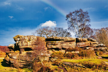 Scenic view of a rocky outcrop with a lone tree against a blue sky with a faint rainbow in the...