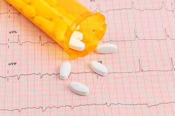 Anti cholesterol pills used for hypertension and heart disease treatment spilled out on an electrocardiogram (ECG) printout
