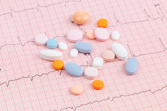 a variety of pills and tablets pills used for hypertension and heart disease treatment spilled out on an electrocardiogram (ECG) printout