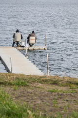 dwóch wędkarzy siedzących na krzesełkach na drewnianym pomoście i łowiących ryby w jeziorze