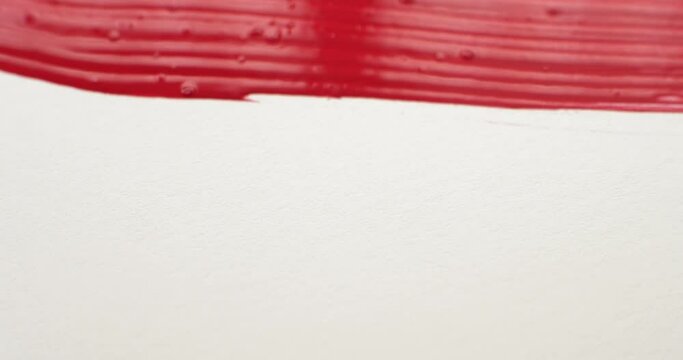 Close up of an artist's paintbrush with brush strokes painting vibrant red paint covering the canvas creating a solid red background.