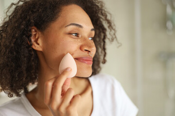 Fototapeta na wymiar a woman is using a sponge to apply makeup to her face