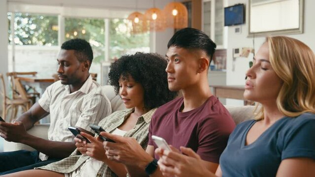 Close up of group of excited multi-racial friends sitting on sofa playing online quiz game on mobile phones together - shot in slow motion
