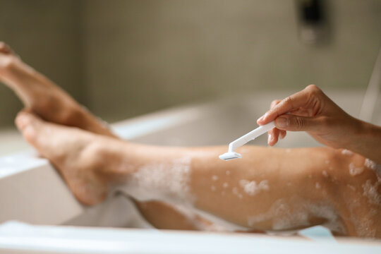 A woman is using a razor to shave her legs in a bathtub