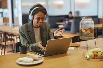 A woman wearing headphones is seated at a table with a laptop computer
