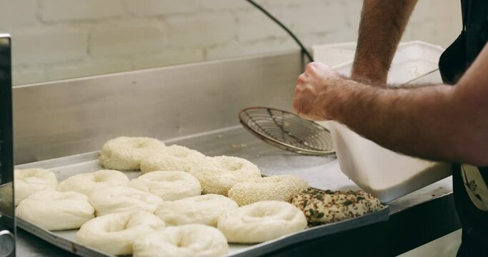 Kitchen, man hands and bagel sesame on stove with chef, food and bread making in a restaurant. Cafe, oil and catering of a professional baker in coffee shop working with dough at small business