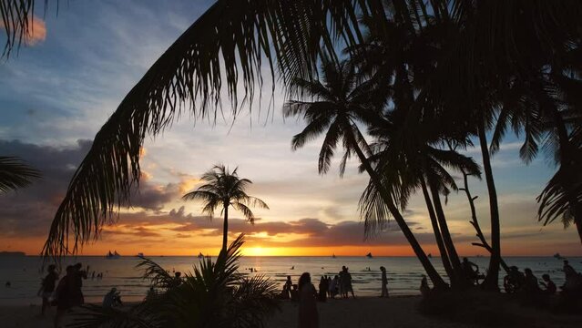 Silhouetted people and palms near sea. Sunset at tropical White beach, Boracay island, Philippines, 4k